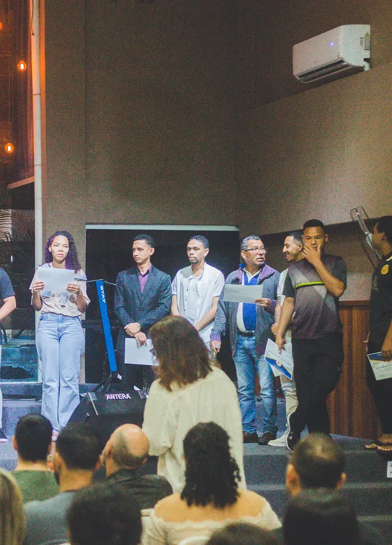 Formandos adultos no palco, segurando o certificado de conclusão