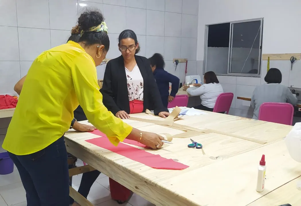 Aula de corte e costura no Instituto: a professora acompanha a aluna que risca o molde na mesa de corte