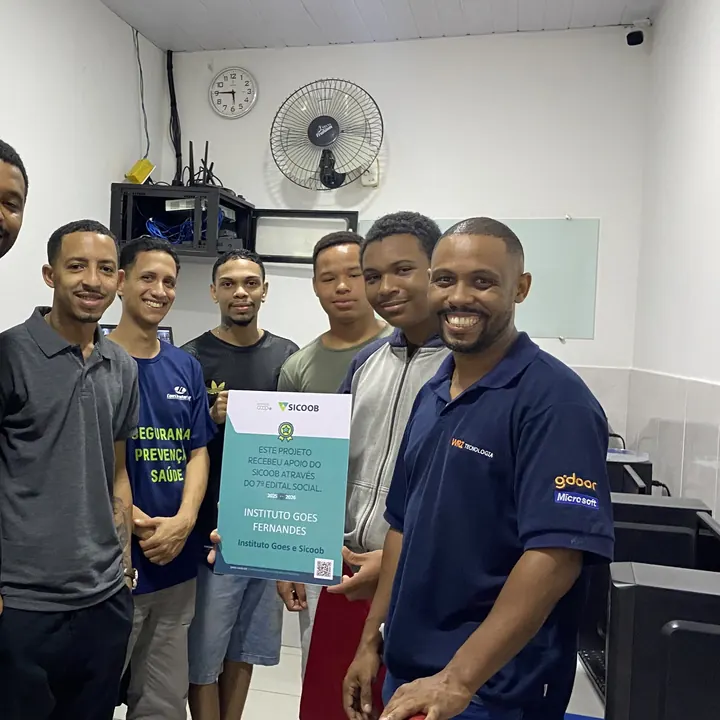 Turma reunida no laboratório de informática, com a placa do projeto