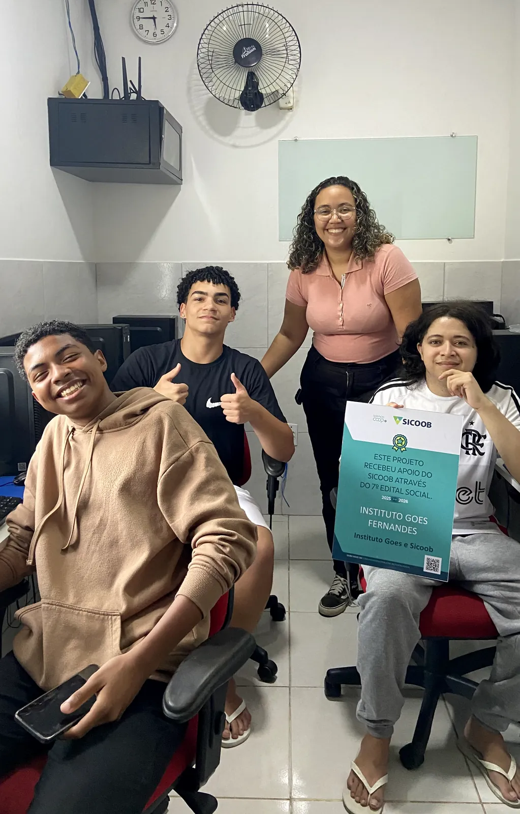 Professora e alunos no laboratório de informática do Instituto, com a placa do projeto