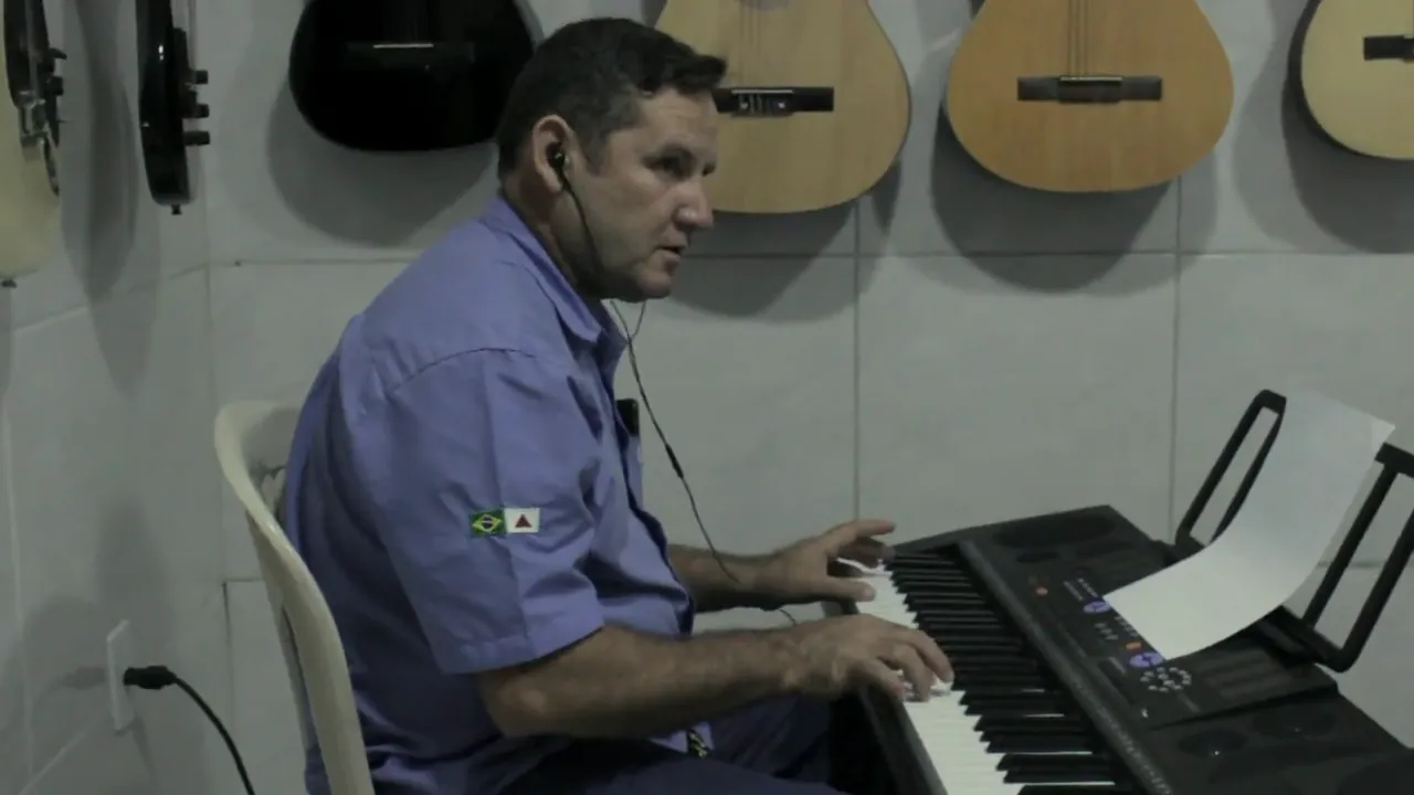 Aluno adulto na aula de teclado, na sala de música do Instituto, com violões pendurados na parede